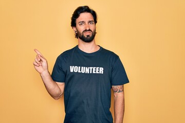 Young handsome hispanic volunteer man wearing volunteering t-shirt as social care Pointing aside worried and nervous with forefinger, concerned and surprised expression