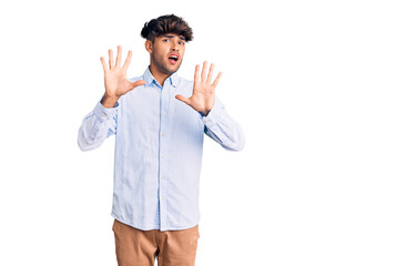 Young hispanic man wearing casual shirt afraid and terrified with fear expression stop gesture with hands, shouting in shock. panic concept.