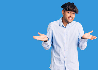 Young hispanic man wearing casual shirt clueless and confused expression with arms and hands...