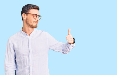 Handsome young man with bear wearing elegant business shirt and glasses looking proud, smiling doing thumbs up gesture to the side