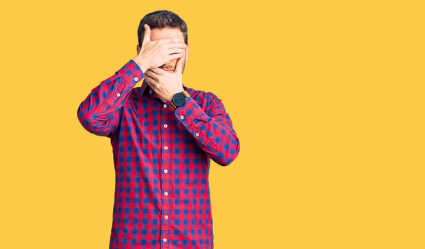 Handsome young man with bear wearing casual shirt covering eyes and mouth with hands, surprised and shocked. hiding emotion