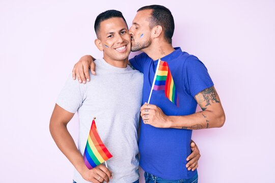 Young couple of gay men together in love holding homosexual pride colorful flag kissing with affection