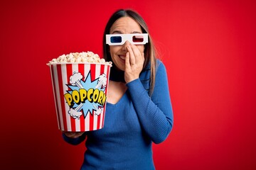 Young blonde woman wearing 3d glasses and eating pack of popcorn watching a movie on cinema...