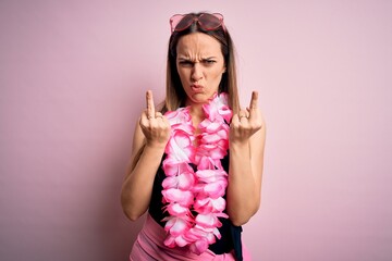 Young beautiful blonde woman wearing swimsuit and floral Hawaiian lei over pink background Showing middle finger doing fuck you bad expression, provocation and rude attitude. Screaming excited