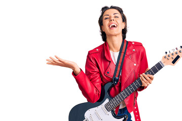 Fototapeta premium Young beautiful woman playing electric guitar celebrating victory with happy smile and winner expression with raised hands