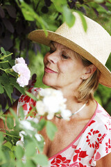 A woman in straw hat and floral blouse sniffing a flower