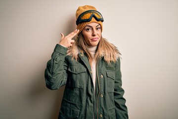 Young brunette skier woman wearing snow clothes and ski goggles over white background Shooting and killing oneself pointing hand and fingers to head like gun, suicide gesture.