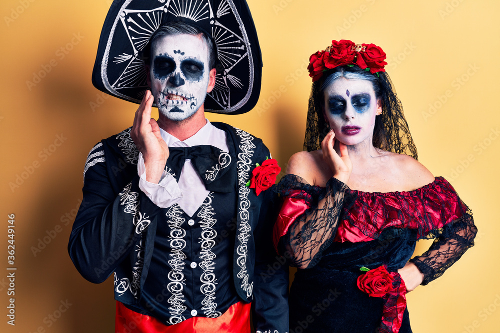 Poster young couple wearing mexican day of the dead costume over yellow touching mouth with hand with painf