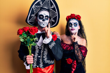 Obraz premium Young couple wearing mexican day of the dead costume holding roses serious face thinking about question with hand on chin, thoughtful about confusing idea