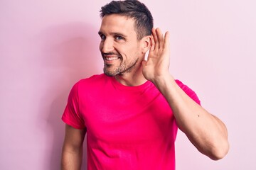 Young handsome man wearing casual t-shirt standing over isolated pink background smiling with hand over ear listening and hearing to rumor or gossip. Deafness concept.