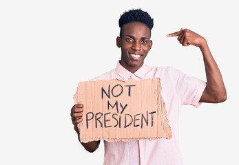 Young african american man holding not my president protest banner pointing finger to one self smiling happy and proud