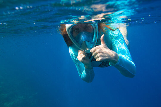 Young woman in snorkeling mask underwater photo. Female snorkel show thumb undersea. Snorkeling in tropical sea