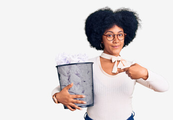 Young african american girl holding paper bin full of crumpled papers smiling happy pointing with hand and finger
