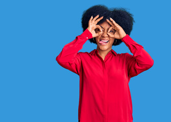 Young african american girl wearing casual clothes doing ok gesture like binoculars sticking tongue out, eyes looking through fingers. crazy expression.