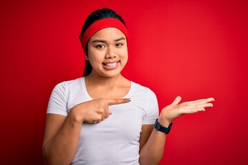 Young beautiful asian sporty woman wearing sportswear doing sport over red background amazed and smiling to the camera while presenting with hand and pointing with finger.