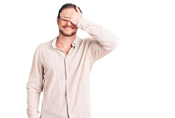 Fototapeta premium Young handsome caucasian man wearing casual clothes smiling and laughing with hand on face covering eyes for surprise. blind concept.