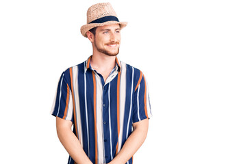 Young handsome caucasian man wearing summer hat looking away to side with smile on face, natural expression. laughing confident.