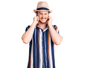 Young handsome caucasian man wearing summer hat covering ears with fingers with annoyed expression for the noise of loud music. deaf concept.