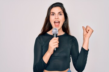 Young beautiful singer performer girl singing using music microphone over isolated background screaming proud and celebrating victory and success very excited, cheering emotion