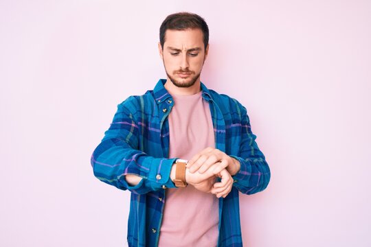 Young handsome man wearing casual clothes checking the time on wrist watch, relaxed and confident