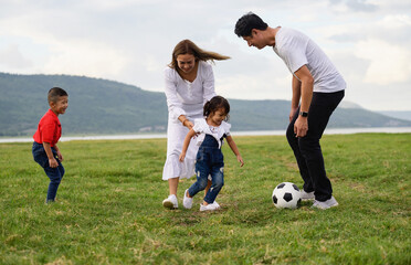 Cheerful family Asian playing football in a green lawn