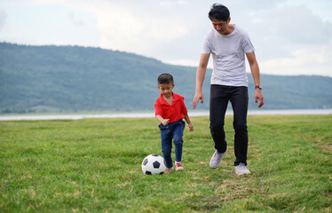 Cheerful family Asian playing football in a green lawn