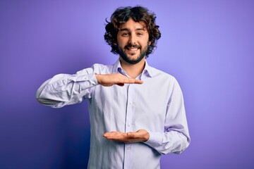Young handsome business man with beard wearing shirt standing over purple background gesturing with hands showing big and large size sign, measure symbol. Smiling looking at the camera. Measuring.