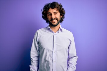 Fototapeta na wymiar Young handsome business man with beard wearing shirt standing over purple background winking looking at the camera with sexy expression, cheerful and happy face.