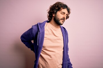 Young handsome sporty man with beard wearing casual sweatshirt over pink background Suffering of backache, touching back with hand, muscular pain