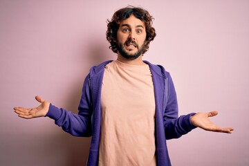 Young handsome sporty man with beard wearing casual sweatshirt over pink background clueless and...