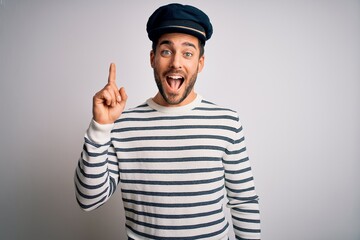 Young handsome sailor man with beard wearing navy striped uniform and captain hat pointing finger...