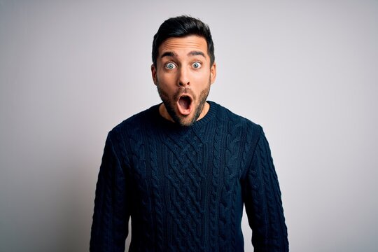 Young handsome man with beard wearing casual sweater standing over white background afraid and shocked with surprise expression, fear and excited face.