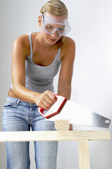 A woman with goggles sawing a wood