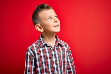 Young little caucasian kid with blue eyes standing wearing elegant shirt over red background looking away to side with smile on face, natural expression. Laughing confident.