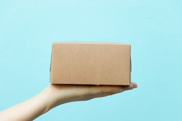 Woman hand hold the brown corrugated box on blue  wall background with copy space
