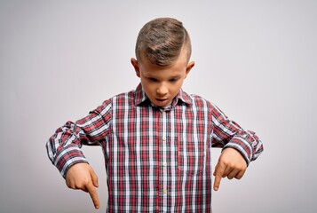 Young little caucasian kid with blue eyes wearing elegant shirt standing over isolated background Pointing down with fingers showing advertisement, surprised face and open mouth