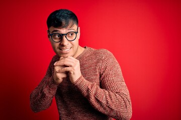 Young handsome hispanic man wearing nerd glasses over red background laughing nervous and excited...