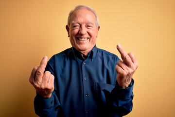 Grey haired senior man wearing casual blue shirt standing over yellow background Showing middle...