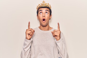 Young african amercian man wearing prince crown amazed and surprised looking up and pointing with...