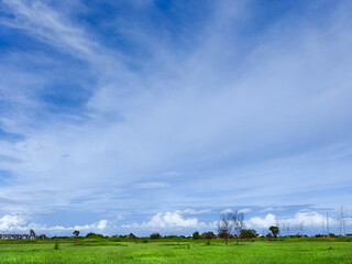 blue sky with white fluffy clouds and grass field near village
