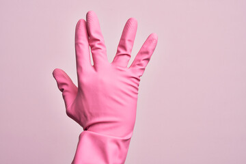 Hand of caucasian young man with cleaning glove over isolated pink background greeting doing Vulcan salute, showing back of the hand and fingers, freak culture