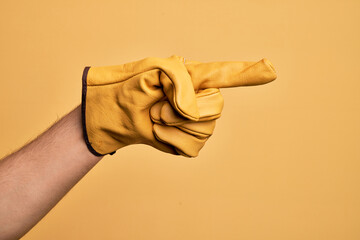 Hand of caucasian young man with gardener glove over isolated yellow background pointing with index finger to the side, suggesting and selecting a choice