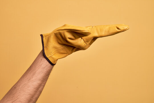 Hand of caucasian young man with gardener glove over isolated yellow background with flat palm presenting product, offer and giving gesture, blank copy space