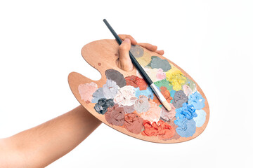 Hand of caucasian young man holding paintbrush and palette with colors over isolated white...