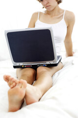 A woman in white camisole sitting on the bed playing with her laptop