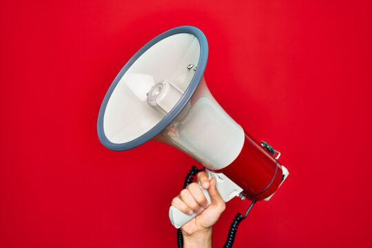 Beautiful hand of man holding megaphone over isolated red background