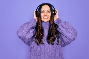 Young beautiful woman with blue eyes listening to music and dancing using headphones with a happy...