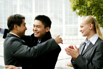 Two men hugging each other while a woman clapping her hands