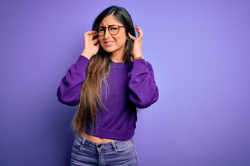 Young beautiful smart woman wearing glasses over purple isolated background covering ears with fingers with annoyed expression for the noise of loud music. Deaf concept.