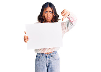 Young beautiful mixed race woman holding cardboard banner with blank space with angry face, negative sign showing dislike with thumbs down, rejection concept